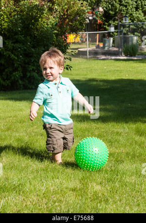 Kleinkind spielt mit grünen Kunststoff-Kugel im Hinterhof, USA Stockfoto