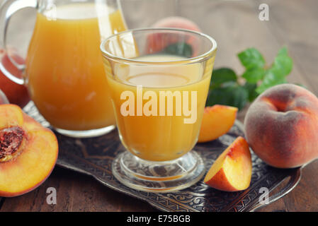 Pfirsichsaft im Krug und Glas mit frischen Pfirsichen auf hölzernen Hintergrund Stockfoto