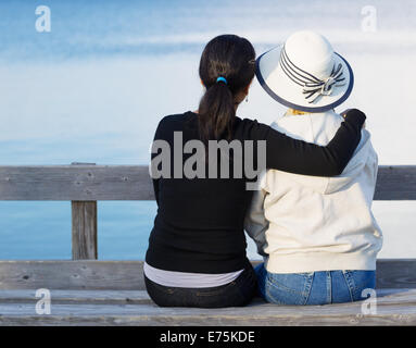 Nahaufnahme von Mutter und ältere Tochter Standortwahl auf Holzbank beim Blick auf den See Stockfoto