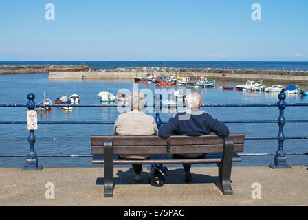 Älteres paar sitzen mit Blick auf die Nordsee Staithes, North Yorkshire, England, UK Stockfoto