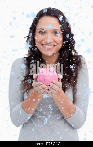 Zusammengesetztes Bild der Piggy Bank durch lächelnde Frau statt Stockfoto