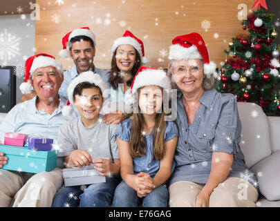 Zusammengesetztes Bild der Großfamilie im Weihnachtsmützen mit Geschenk-Boxen im Wohnzimmer Stockfoto