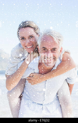 Zusammengesetztes Bild des Mannes mit seiner lächelnden Frau Huckepack am Strand Stockfoto