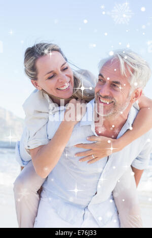 Zusammengesetztes Bild des Mannes mit seiner lächelnden Frau Huckepack am Strand Stockfoto
