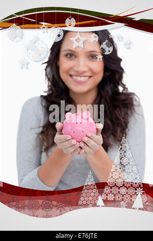 Zusammengesetztes Bild der Piggy Bank durch lächelnde Frau statt Stockfoto