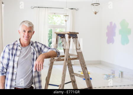 Älterer Mann lächelnd in der Nähe von Leiter im Wohnzimmer Stockfoto