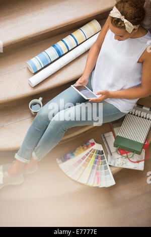 Frau mit digital-Tablette auf Treppe umgeben von Wand Papier und Farbe Farbfelder Stockfoto