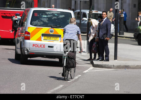 Ein Radfahrer hinter einen Polizeiwagen und andere Verkehrsmittel in London unterwegs. Fußgänger warten, um die Straße zu überqueren Stockfoto