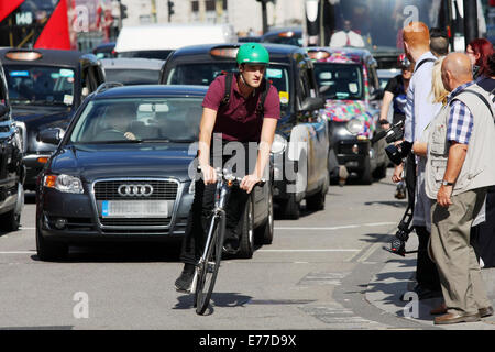 Ein Radfahrer führt eine Warteschlange von Verkehr in London in einer Kurve warten Fußgänger die Straße überqueren Stockfoto