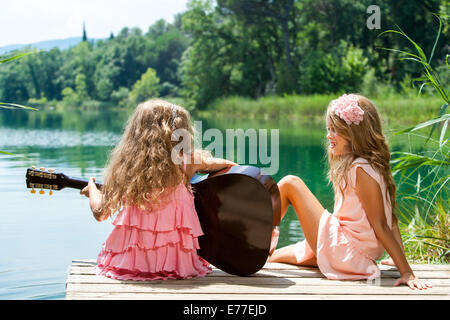 Junge Mädchen singen zusammen mit spanischer Gitarre am See. Stockfoto