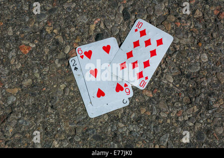 Drei Karten, zwei Pik, sechs von Herzen und zehn Diamanten auf einer asphaltierten Straße gefunden. Stockfoto