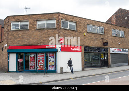 Ein behinderter Mann auf Krücken geht vorbei an einem Ladbrokes Wetten shop Stockfoto