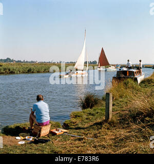 Angeln am Ufer des Flusses Thurne, Norfolk, mit Booten über Mann Stockfoto