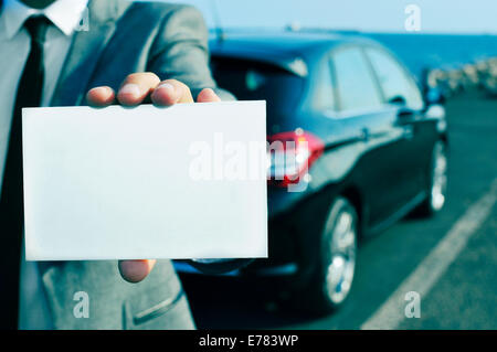 Nahaufnahme eines Mannes im Anzug hält eine leere Schild mit einem Auto im Hintergrund Stockfoto