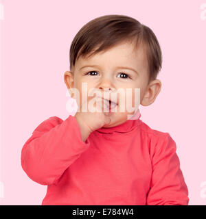 Entzückende Babymädchen mit der Hand im Mund auf rosa Hintergrund isoliert Stockfoto