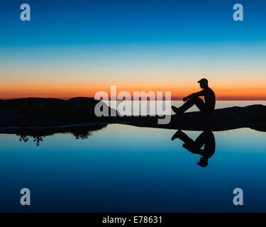 Silhouette eines Mannes sitzt ein Gezeiten-Pool bei Sonnenuntergang Stockfoto