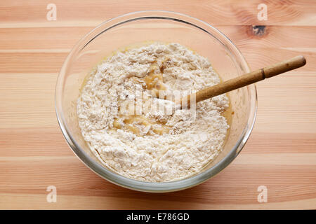 Mehl wird in feuchten Teig für Bananen Brot in eine Glasschüssel auf einem Holztisch gerührt Stockfoto