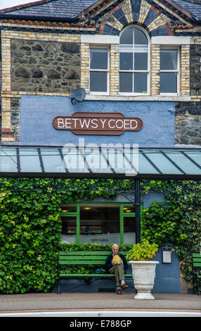 Mann auf Bank warten auf Zug in Betws-y - Coed Railway Station Nord-Wales Stockfoto