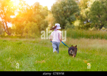 Kleines Mädchen mit Hund auf der Wiese laufen und halten den Hund an der Leine zurück zu Kamera Stockfoto