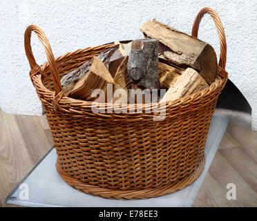 Weidenkorb von Brennholz auf dem Boden in der Nähe von weißen Ofen Stockfoto