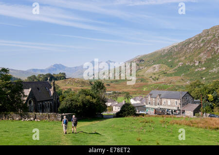 Blick auf das Dorf mit zwei Wanderer zu Fuß hinunter den Hang In Snowdonia-Nationalpark. Capel Curig, Conwy, North Wales, UK, Großbritannien Stockfoto