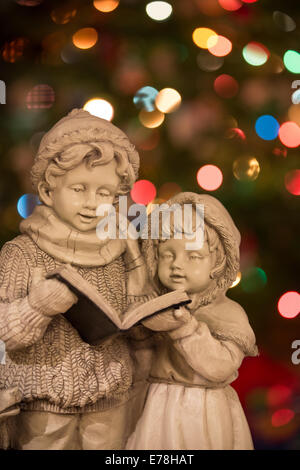 Statue von Weihnachten Kurrende / Sänger vor der Weihnachtsbaum mit Lichtern unscharf gestellt. Stockfoto