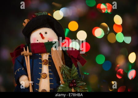 Schneemann-Puppe mit Holzskier vor Weihnachtsbaum Lichter, die absichtlich unscharf sind. Stockfoto