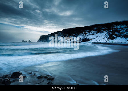 der schwarze Sandstrand bei Vík Í Mýrdal im Winter, mit den Renisdrangar Basalt Felsnadeln über Süden Islands Stockfoto