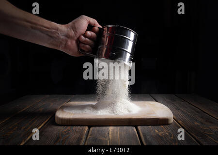 Hand siebt das Mehl durch ein Sieb passieren. Stockfoto