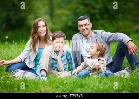 Glückliche Familie Blick in die Kamera beim Sitzen im grünen Rasen im freien Stockfoto