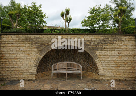 Eine geschwungene Holzbank neben einer Cotswold-Steinmauer mit einer halbrunden Nische im ländlichen Gloucestershire, England, Großbritannien Stockfoto