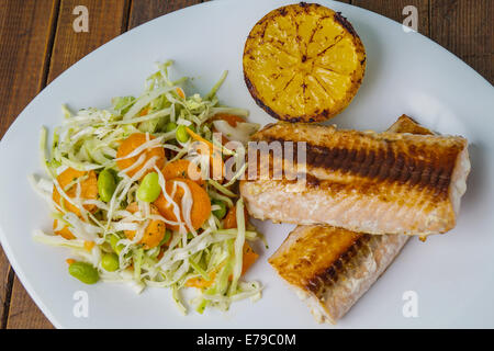 Lachs mit Salat und Zitrone, serviert auf einem weißen Teller Stockfoto