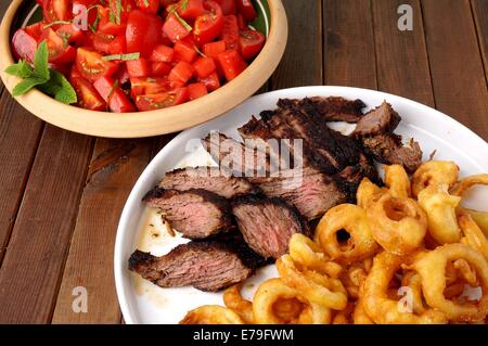 Flanke Steak mit Pommes frites in Ringe geschnittenen Zwiebeln und Salat Stockfoto