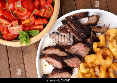 Flanke Steak mit Pommes frites in Ringe geschnittenen Zwiebeln und Salat Stockfoto