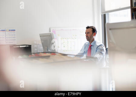 Ein Mann sitzt an einem Schreibtisch mit einem Computer. Eine Wandkarte mit post-it Klebefuge Notizen. Stockfoto
