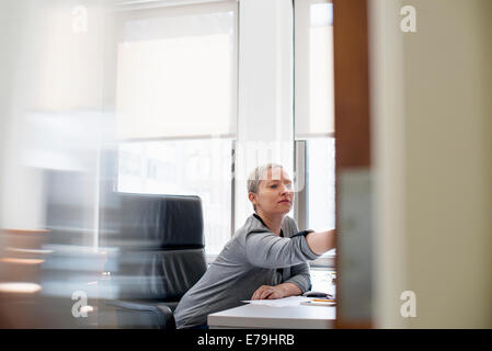 Eine Frau arbeitet in einem Büro alleine an ihrem Schreibtisch nach vorne lehnen, um etwas zu betrachten. Stockfoto