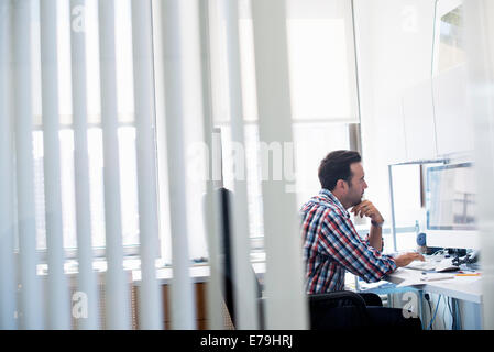 Ein Mann in einem Büro arbeiten auf eine Aufgabe konzentrieren. Mit Hilfe einer Computer-Tastatur und Bildschirm. Stockfoto