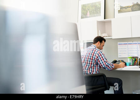 Ein Mann in einem Büro an einem Schreibtisch mit einem Computer arbeiten. Stockfoto