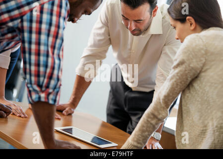 Vier Personen stützte sich auf einen Tisch bei einem Treffen, suchen in ein digital-Tablette. Stockfoto