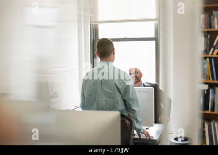 Büroalltag. Zwei Menschen, Geschäftsleute, die über ihre Schreibtische miteinander zu reden. Stockfoto