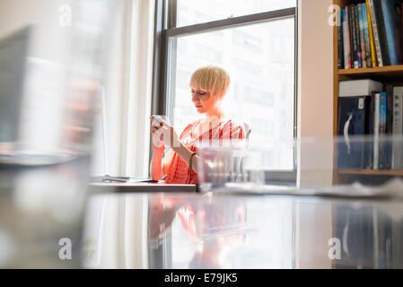 Büroalltag. Eine junge Frau, die ihr Handy überprüfen. Stockfoto