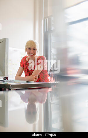 Büroalltag. Eine junge Frau sitzt an einem Büro Schreibtisch Lächeln auf den Lippen. Stockfoto
