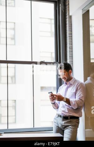 Büroalltag. Ein Mann in einem Büro sein Smartphone überprüfen. Stockfoto