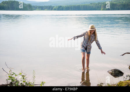 Ein junges Mädchen in einem Strohhut und Shorts Paddeln im flachen Wasser eines Sees. Stockfoto