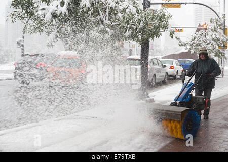 Calgary, Alberta, Kanada, 10. September 2014. Frau räumt Schnee aus dem Bürgersteig in der Kensington Nachbarschaft als fallenden Schnee bedeckt die Stadt. Calgarys Notfallzentrale wurde als Reaktion auf den Spätsommersturm eröffnet. Bürgermeister Nenshi kündigte auf Twitter an, dass die 3 Prioritäten die öffentliche Sicherheit, die Wiederherstellung von Strom und die Beseitigung von Trümmern sind. Quelle: Rosanne Tackaberry/Alamy Live News Stockfoto