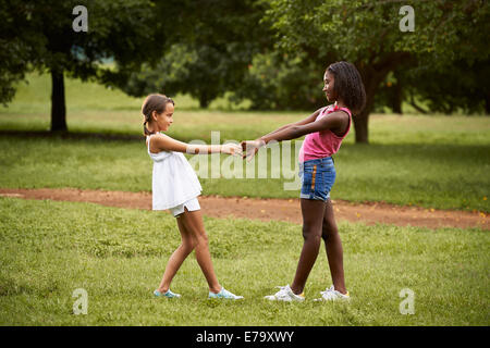 Zwei spanische und afrikanische Mädchen spielen Ring um den Rosie im öffentlichen Park und Hand in Hand Stockfoto