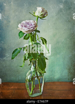 Zwei rosa Rosen in einem Glas auf einem hölzernen Tisch und Grunge Textur Stockfoto