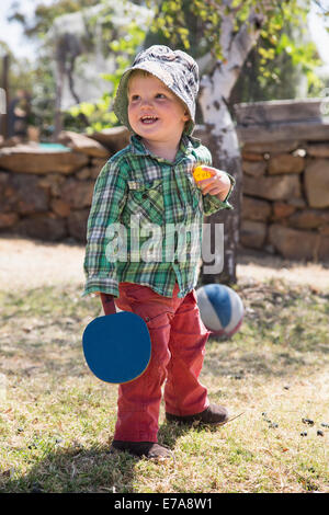 Fröhlicher Junge hält Tischtennisschläger und Ball im park Stockfoto
