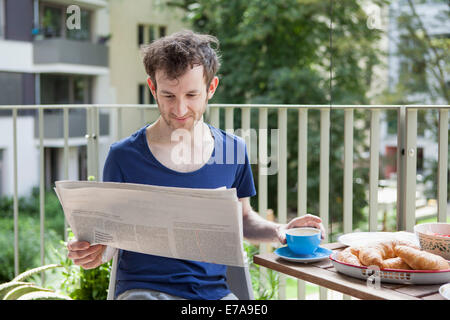 Junge Mann liest Zeitung beim Frühstück auf der Veranda Stockfoto