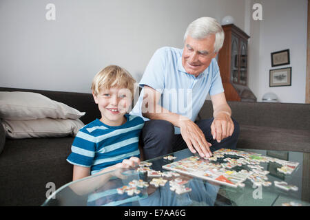 Porträt von glücklichen Enkel Lösung Puzzle mit Großvater im Wohnzimmer zu Hause Stockfoto